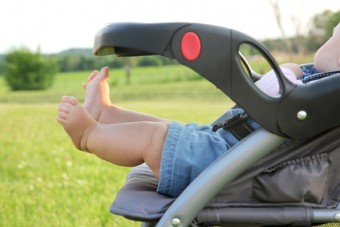 The cute, chubby legs of a newborn baby girl are sticking out of a stroller while on a walk outside in the country.