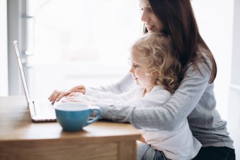 Young mother and her little daughter sitting on kitchen using a laptop
